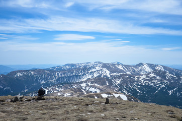 Man sitting alone, looking at the beautiful mountain snowy peaks during sunny day, Carpathian mountains, Ukraine. Man traveler sitting on rock at mountain top after long hike.