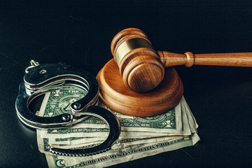 Bribe concept. Dollar banknotes, handcuffs and gavel on dark black table