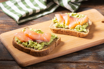 Bruschetta with avocado and salmon on a wooden Board on a brown wooden table. Toasted bread with avocado and red fish. The concept is useful and delicious Breakfast