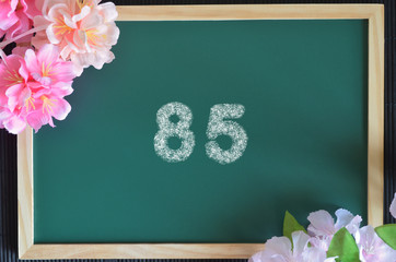 Number 85 write with white chalk, flowers on the board.