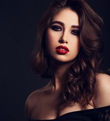 Beautiful bright makeup woman with long brown curly volume hair style, red lipstick, and black smokey eyes looking on grey background. Closeup