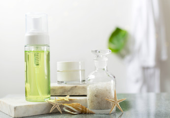 Closeup of bottles of gel, sea salt, cream for face, sea stars and shell on the bath shelf, bathrobe hanging on the wall.Concept of relaxation treatments