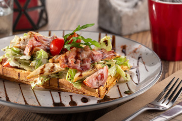 Belgian waffles with egg, arugula, tomatoes and meat. Delicious breakfast: fried egg, waffles, bacon, beans and salad close-up on a plate.