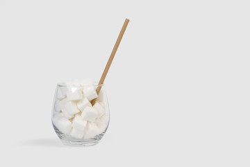 Terrones de azúcar blanco dentro de un vaso de cristal con pajita sobre fondo gris liso claro. Vista de frente. Copy space