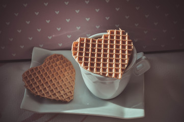 Valentine's day romantic postcard with a cup of coffee and two waffle hearts on a pink background of hearts