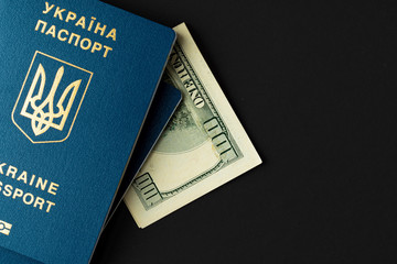 Ukrainian passport with US dollars banknotes on black background