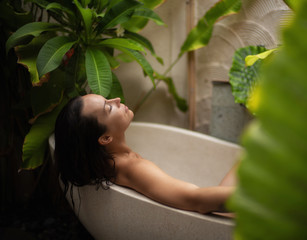 Woman relaxing in outdoor bath with tropical leaves at Bali