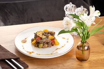 Delicious fresh salad. Warm salad with veal, tomatoes, peppers, lettuce on wooden background served with wine. Restaurant food, close up. Meat salad. Close up view on Salad with warm baked veal.