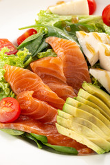 Delicious fresh salad. Salad with salmon, avocado, lettuce, tomatoes, parmesan, cheese, spinach. Fresh salmon salad with avocado and vegetables. Close up view on Salad