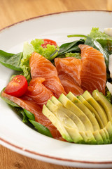 Delicious fresh salad. Salad with salmon, avocado, lettuce, tomatoes, parmesan, cheese, spinach. Fresh salmon salad with avocado and vegetables. Close up view on Salad