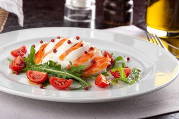 Delicious fresh salad. Salad with salmon, mozzarella cheese, cherry tomatoes, arugula, olive oil. Fresh salmon salad with mozzarella and vegetables. Close up view on Salad. Healthy, diet tasty summer 