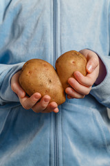 A little girl is holding in front of herself an ugly potato in the shape of a heart. Vertical...