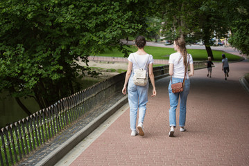 Fototapeta na wymiar Two girlfriends go to alley of the park. Students in the summer walk in the Park. Back view