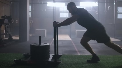Motivation concept, young athletic blonde man pushing heavy training sled towards camera training in gym slow motion - Powered by Adobe