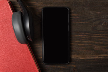 Mobile phone, book and headphones in close-up. Top view of wooden background.