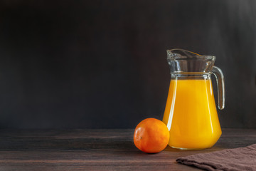 Orange juce in glass decanter with orange on dark brown wooden background. Horizontal orientation. Copy space. 