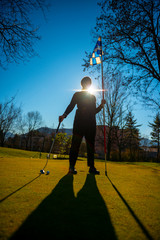 Golfer on the Putting Green and Holding the Golf Flag and Golf Putter with Sunlight.