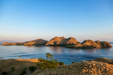 Fototapeta premium A view on a the morning sun rising over an island formation in Komodo National Park, Flores, Indonesia. Golden hour over the islands and sea. Idyllic landscape. New day beginning. Chocolate hills.