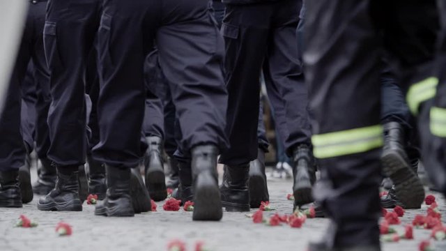 Close up of military men maching on cobblestone and stepping over red carnations