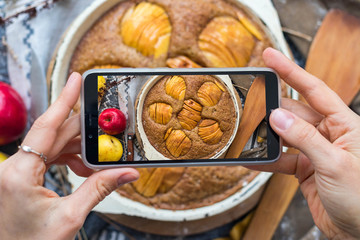Woman take a picture of apple pie or cake using phone at her kitchen. Vegan healthy dessert. Smartphone food photography