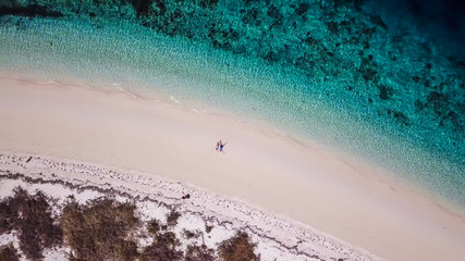 A drone shot of a couple sitting on a pink sand beach on a small island near Maumere, Indonesia. Happy and careless moments. Waves gently washing the shore. Romance and love while travelling