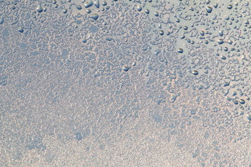 Blue window glass covered hoarfrost ice pattern texture with water drops. Cold nature winter background