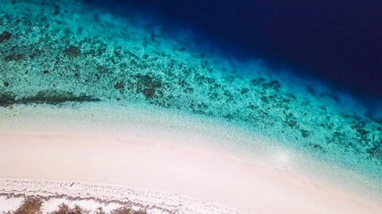A drone shot of a pink sand beach on a small island near Maumere, Indonesia. Happy and careless moments. Waves gently washing the shore.Clear, turquoise coloured water displaying coral reef.