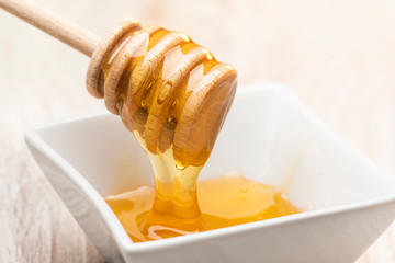 Take honey from a white bowl with wooden dipper.