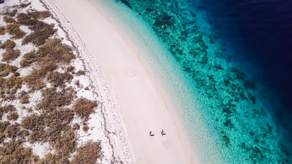 A drone shot of a couple playing on a pink sand beach on a small island near Maumere, Indonesia. Happy and careless moments. Waves gently washing the shore. Romance and love while travelling