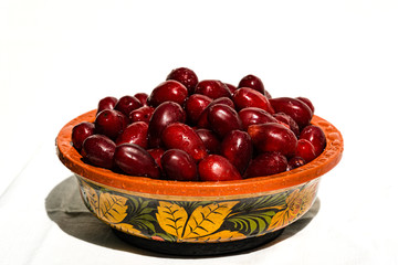 Dark red dogwood berries in wooden bowl on white background. Selective focus.  Wooden bowl is painted with old Khokhloma decorative painting. Bunch of attractive oblong ripe dogwood berries. Calmness.