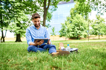 Fototapeta premium Happy young man using tablet while sitting outdoor in the park