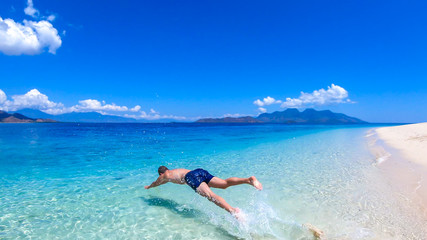 Fototapeta na wymiar A man in swimsuit jumping into a crystal clear sea water on an island near Maumere, Indonesia. Clear, turquoise coloured water displaying coral reef. Happiness and fun while travelling. Hidden gem.