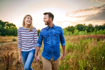 Smiling couple walking through meadow on sunny day and holding hands