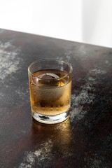 wet glass with strong whiskey and ice cube on black surface