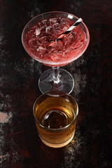 top view of glass with whiskey near red cosmopolitan cocktail on black surface
