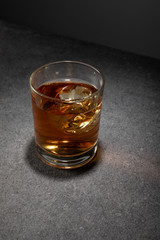 ice cubes in glass of brandy on grey surface