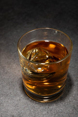 ice cubes in glass of alcoholic drink on grey surface