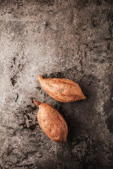 top view of tasty healthy whole sweet potatoes and peeler on grey surface