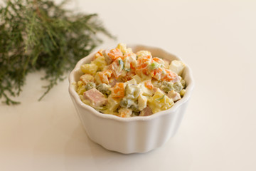 Olivier in a white plate on a pale pink background. the winter salad.ingredients: cucumber, sausage, meat, mayonnaise, sour cream, potatoes, peas, egg. space for your text.