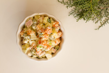 Fototapeta na wymiar Olivier in a white plate on a pale pink background. the winter salad.ingredients: cucumber, sausage, meat, mayonnaise, sour cream, potatoes, peas, egg. space for your text.