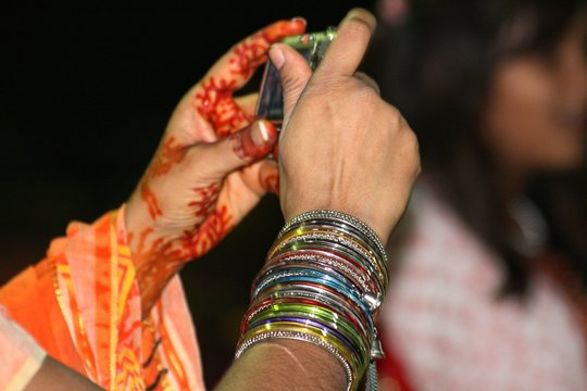 Hand of a woman with henna tattoo and red bangles taking photos with a handheld camera