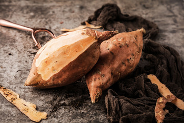 top view of tasty healthy whole sweet potatoes and peeler on grey surface