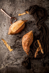 top view of tasty healthy whole sweet potatoes and peeler on grey surface