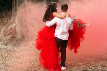 Beautiful romantic couple Attractive young woman in red dress and crown with handsome man in white shirt are dancing on pink smoke.Baby gender Happy Saint Valentine's Day.Pregnant and wedding concept.