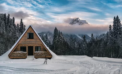 Fotobehang Wooden house at mountain peak and clouds background. Panoramic view of winter landscape at sunset time. Anchkho mount in Abkhazia © lilkin