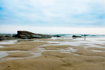 Fototapeta na wymiar Playa de las catedrales en un gran angular con chica al fondo y rocas en la arena