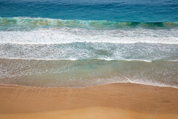 Aerial view of a golden yellow beach where waves crushes, produce white foam  with colorful water blue turquoise azure aquamarine