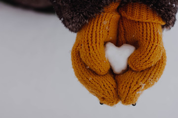 hands in mittens make a heart out of snow