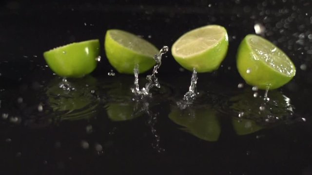 Lime Slices falling onto ground and splashing into water  in Super Slow Motion. Black Background. 