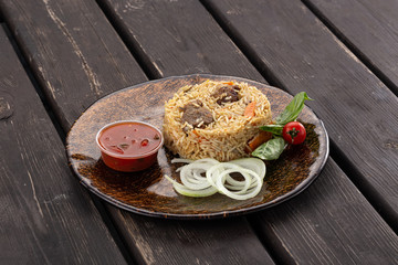 National Uzbek pilaf with meat in a cast-iron skillet, on a wooden table. Traditional asian dish - pilaf from from rice, vegetables and meat in a plate